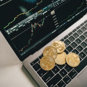 Golden bitcoin coins placed on a laptop keyboard with trading chart displayed on the screen.